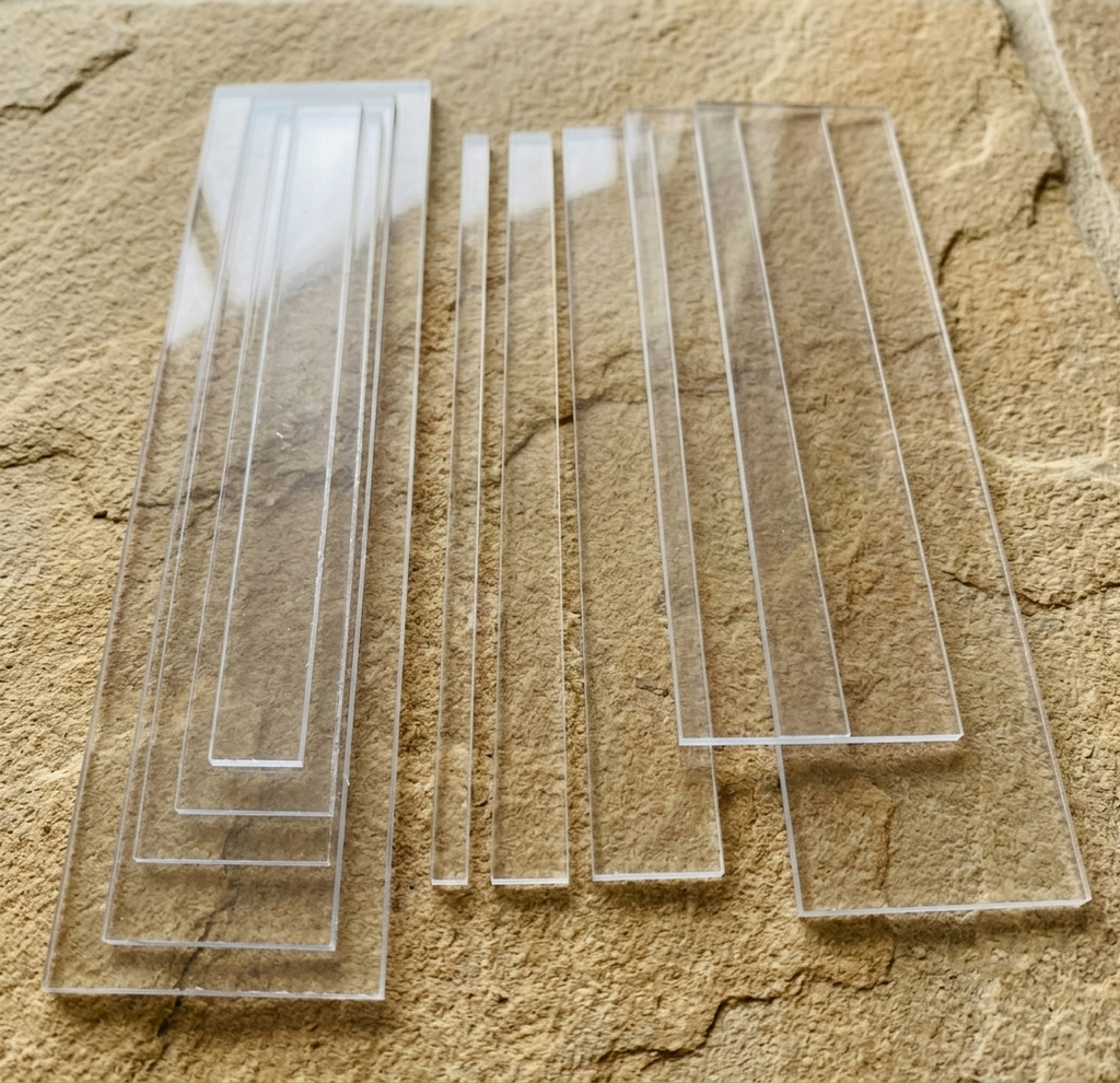 A set of clear acrylic Perspex rectangular strips of varying widths arranged on a textured beige stone surface.