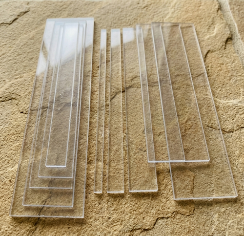 A set of clear acrylic Perspex rectangular strips of varying widths arranged on a textured beige stone surface.