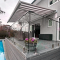A modern outdoor patio with clear glass panels and a gray striped canopy, installed on a gray composite deck next to a swimming pool. Clear angled acrylic panels are covering a gap at the bottom of the glass and balcony floor.