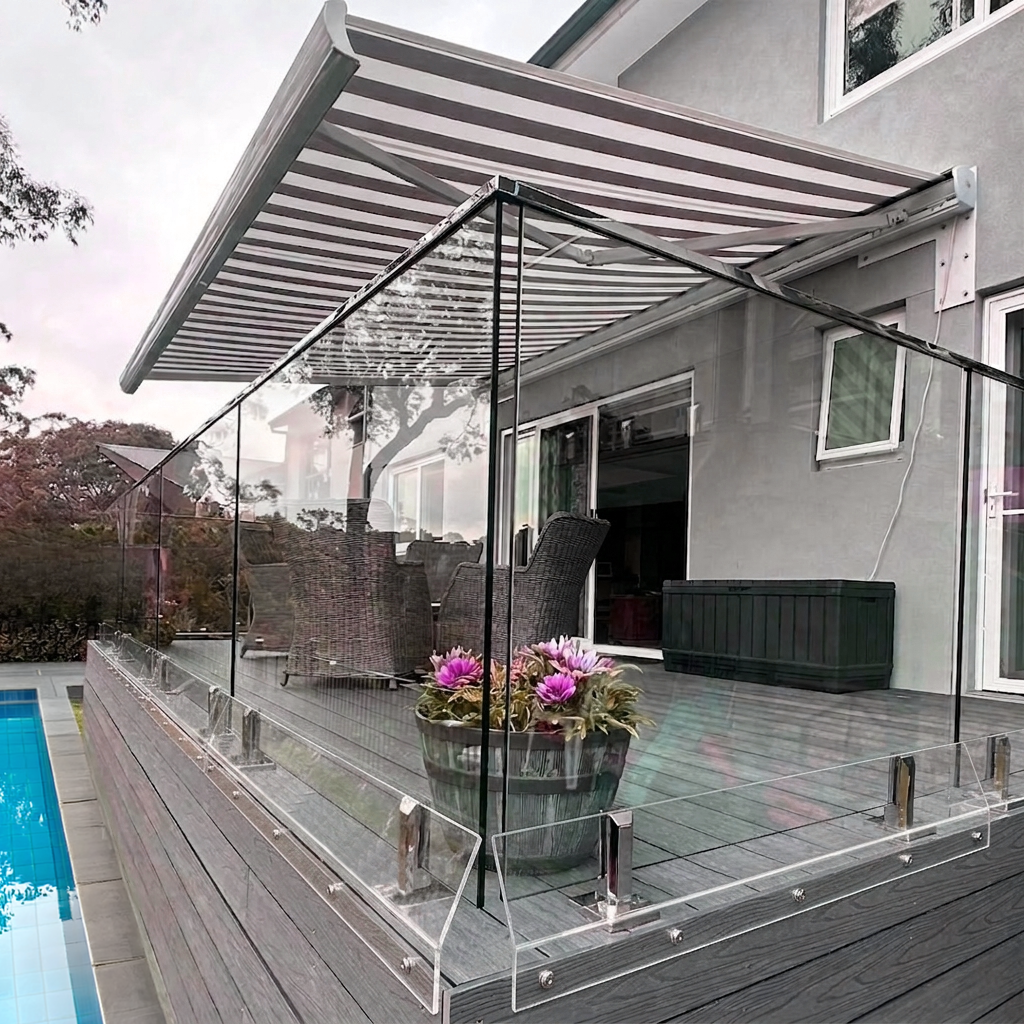 A modern outdoor patio with clear glass panels and a gray striped canopy, installed on a gray composite deck next to a swimming pool. Clear angled acrylic panels are covering a gap at the bottom of the glass and balcony floor.