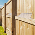 A clear plastic fence guard or cover mounted on a wooden garden fence, shown outdoors with grass and blue sky visible.