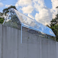 A clear acrylic Perspex teepee mounted on a gray concrete wall outdoors, with trees and a blue sky with clouds visible in the background.
